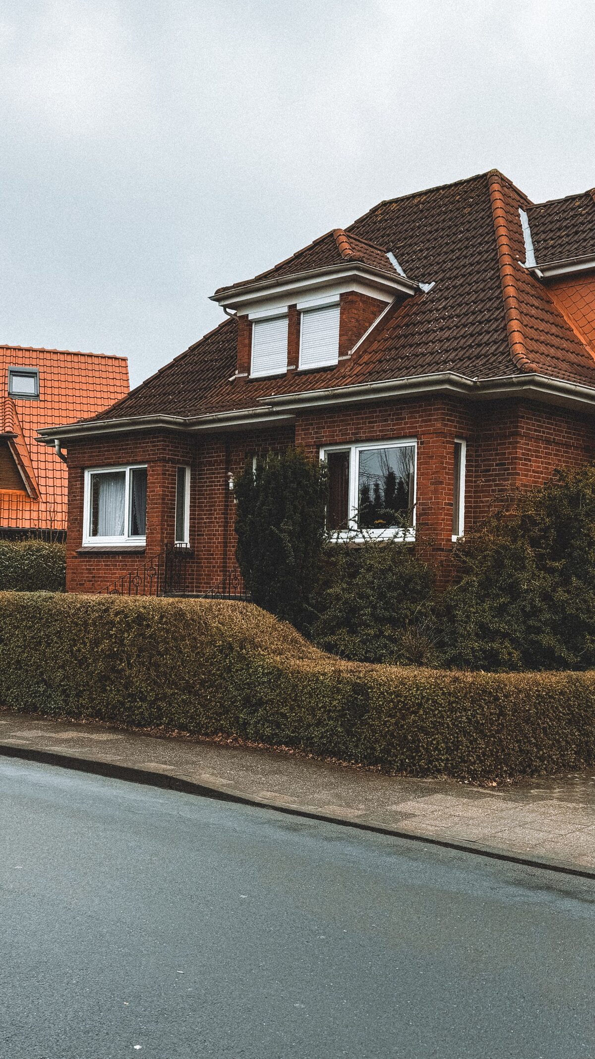 Red brick family home with a tiled roof behind a trimmed hedge