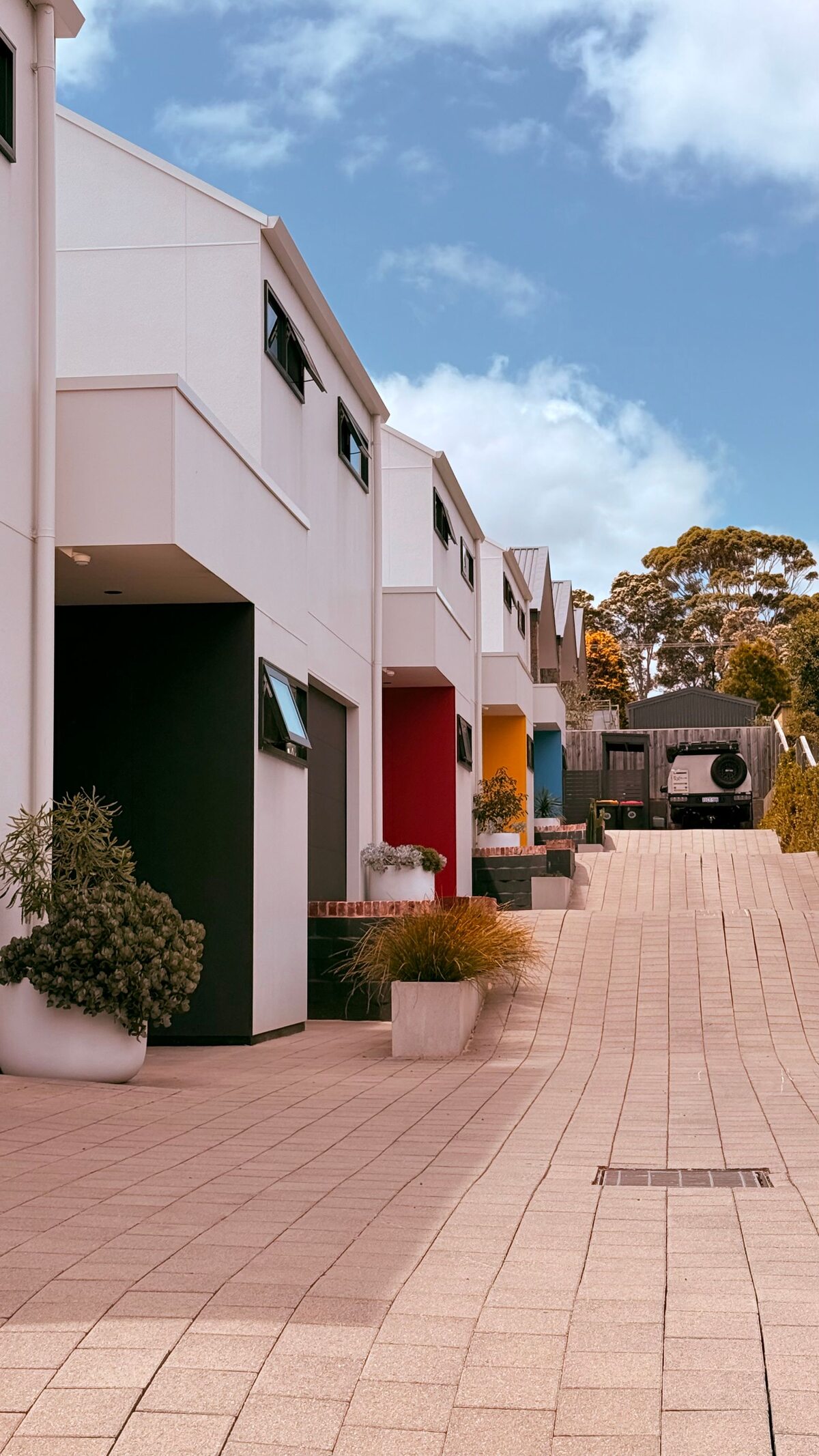 Row of white townhouses with coloured entry doors on a paved driveway